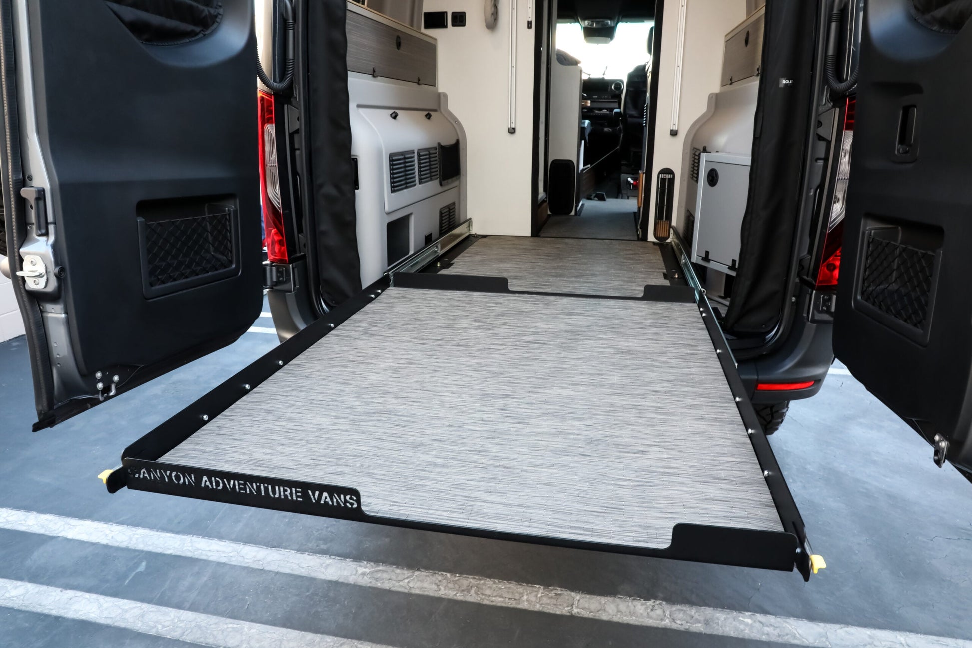 Van interior with a deployed storage ramp labeled Camper Adventure Vans