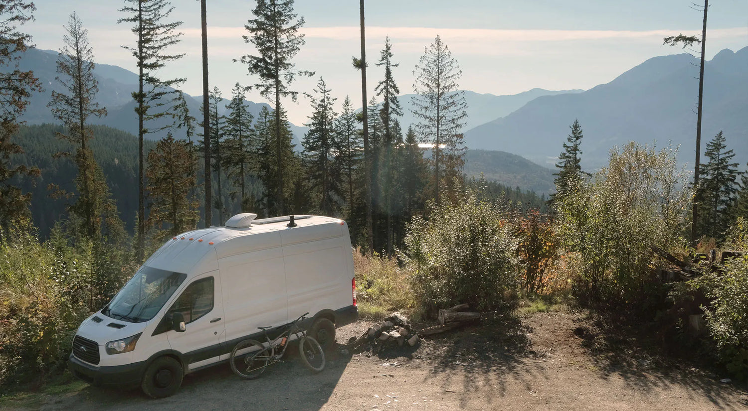 White van parked on a dirt road with mountains and trees in the background